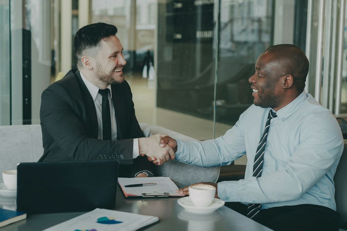 Two business owners shaking hands across a meeting table